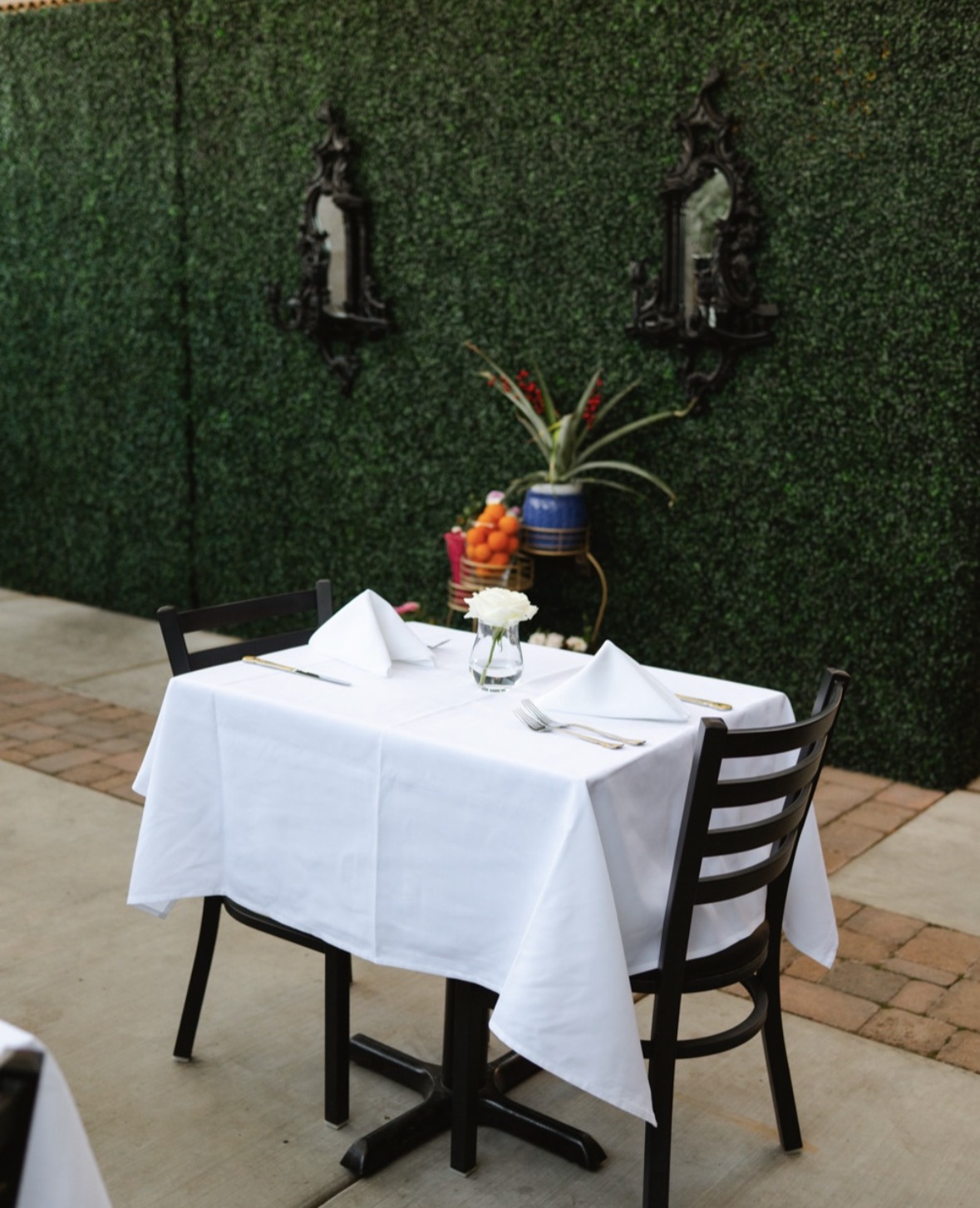 Casa Madre patio table set for two against lush green hedge wall